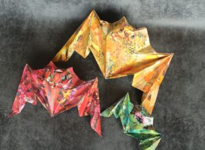 Trois chauves souris en origami recouvert de papiers collés. Une rouge, une verte, une jaune.